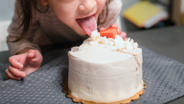 Little girl licking the top of a cake.