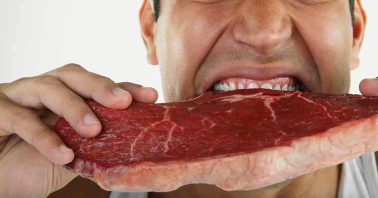 A man biting into a raw steak.