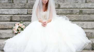 Bride sitting on stone steps, looking towards ground.