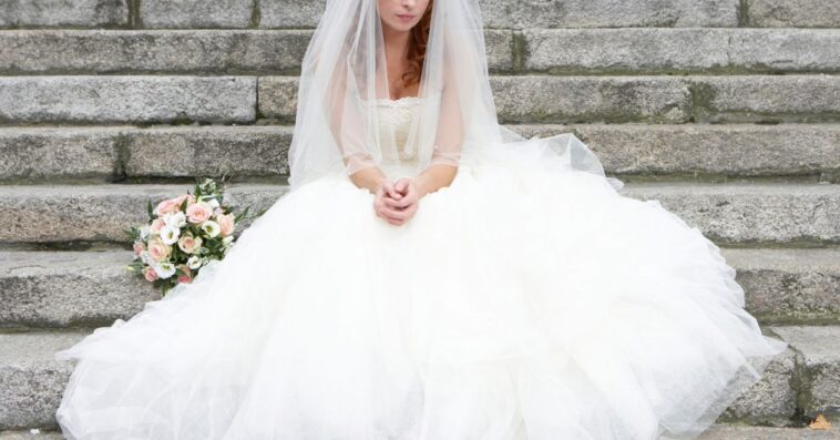 Bride sitting on stone steps, looking towards ground.