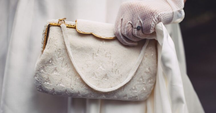 Bride holding white beaded purse bag. Pouch has gilded elements. Close-up.
