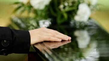 Close up of a female hand on a coffin saying goodbye at an outdoor funeral ceremony