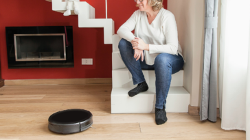 older woman seated on stairs watching robot vacuum