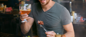 man drinking beer and eating steak