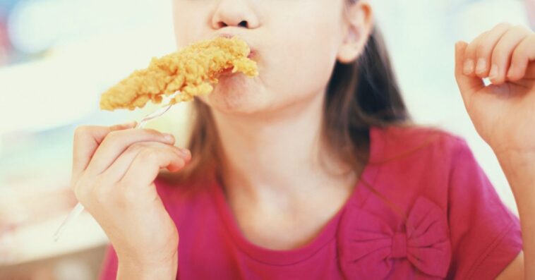 Close-up front view of cute little girl eating fried chicken and yes, enjoying it.