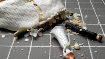 Bride and groom figurines lying at destroyed wedding cake on tiled floor.