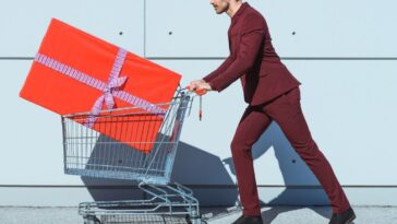 Man in a red suit pushing shopping cart with big red gift box