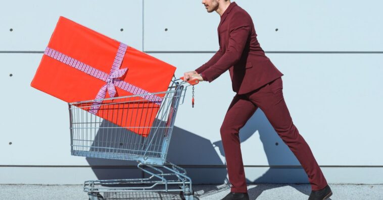 Man in a red suit pushing shopping cart with big red gift box