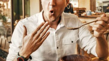 Funny man tries a spicy and hot dish from the national cuisine. He's all red and is trying to cool his mouth with his hand.