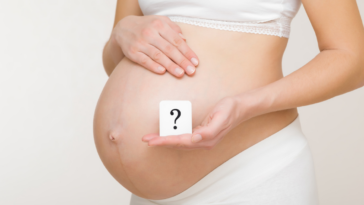 Woman holding a question mark in front of her pregant belly.