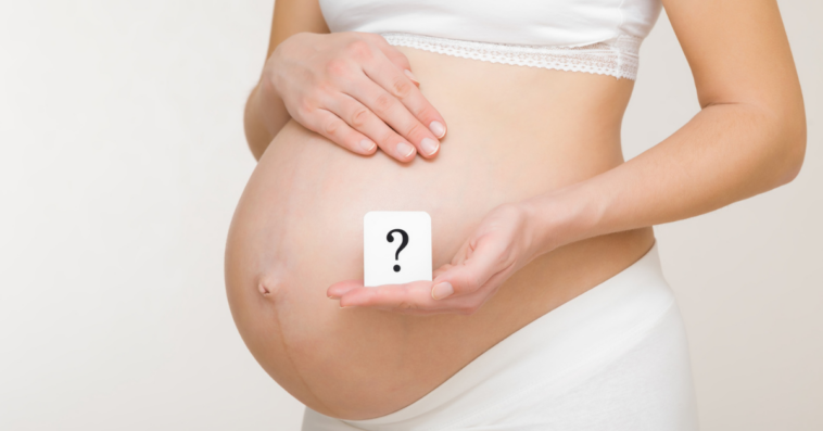 Woman holding a question mark in front of her pregant belly.
