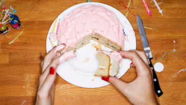 A woman holding a slice of cake with pink icing.