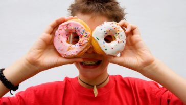 Child holding donuts over their eyes.
