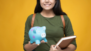 College student holding supplies and a piggy bank