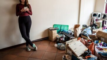 Young woman using mobile phone during house moving at the new apartment.