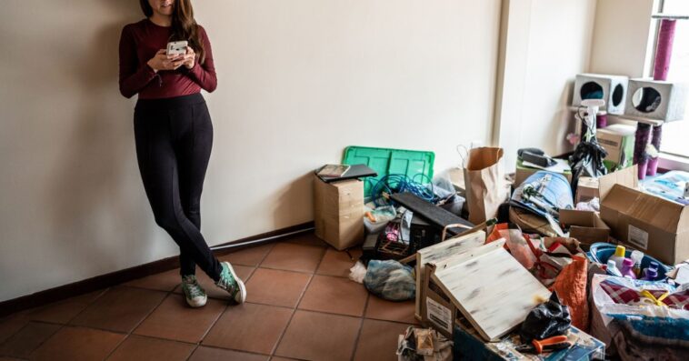 Young woman using mobile phone during house moving at the new apartment.