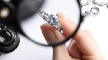 Jeweler examining diamond ring with magnifying glass at white table, closeup.