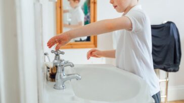A young red headed boy stands in his bathroom about to wash his hands.