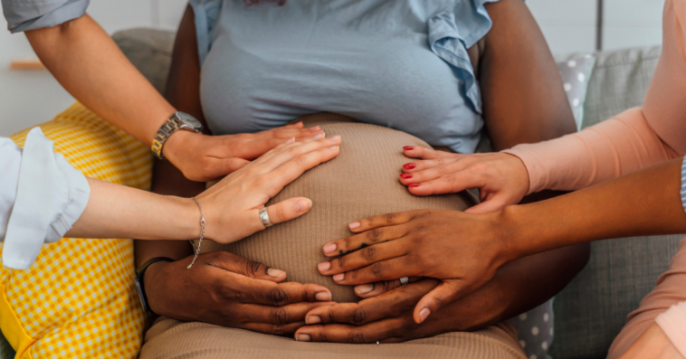 Lots of hands touching a pregnant woman's stomach.
