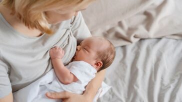 Mother breastfeeding newborn son in arms on bed.