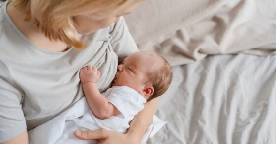 Mother breastfeeding newborn son in arms on bed.