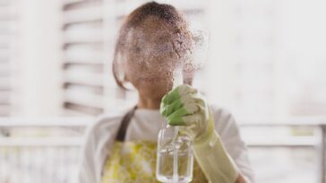 A woman with goggles sprays cleaner on glass, directly facing the camera.