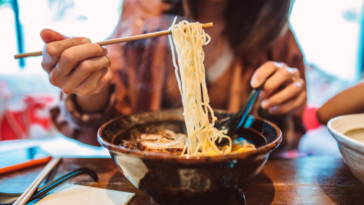 A woman eating a bowl of ramen noodles.