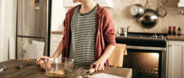Teenager stands at kitchen island with a bowl of eggs in front of him.