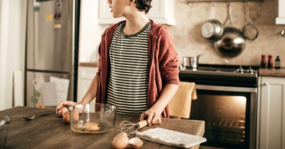Teenager stands at kitchen island with a bowl of eggs in front of him.