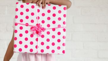 Mixed race sweet little girl holding a square gift, wrapped in white paper that has pink dots, with a pink bow.