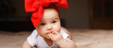 Beautiful little girl lying on the bed with a red bow on her head. Smiling and, happy 3-4 months old.