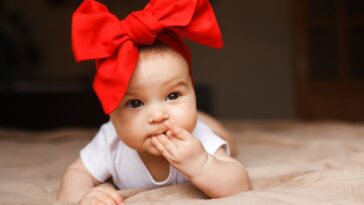 Beautiful little girl lying on the bed with a red bow on her head. Smiling and, happy 3-4 months old.
