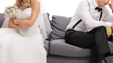 Newlywed coupe sitting on a sofa angry at each other, possibly in a middle of an argument, with an isolated white background.