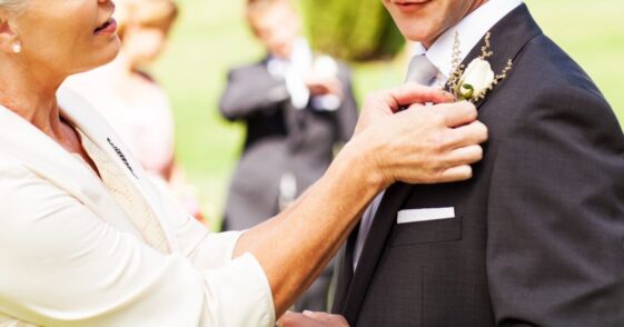 Side view of mother pinning boutonniere on groom's suit at garden wedding.