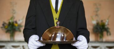 Adult male butler holding serving tray in formal parlor.