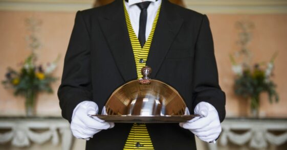 Adult male butler holding serving tray in formal parlor.