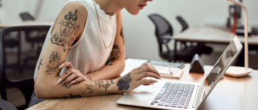 young woman with multiple tattoos working on laptop