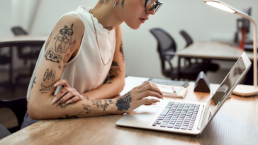 young woman with multiple tattoos working on laptop