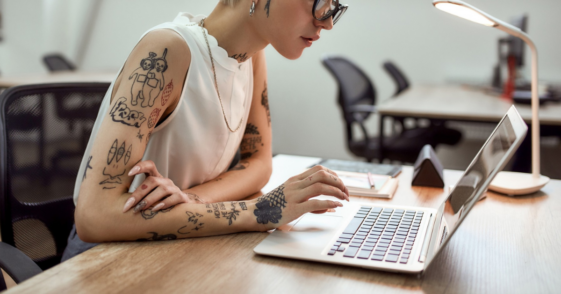 young woman with multiple tattoos working on laptop