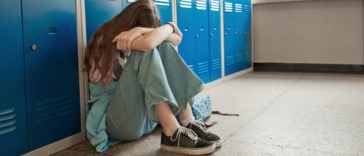 upset teenage girl seated in school hallway in front of lockers