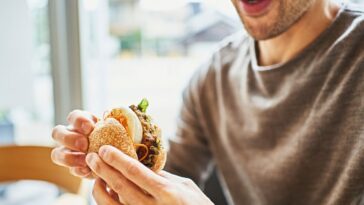 Asian man eating a veggie burger at a vegan cafe.