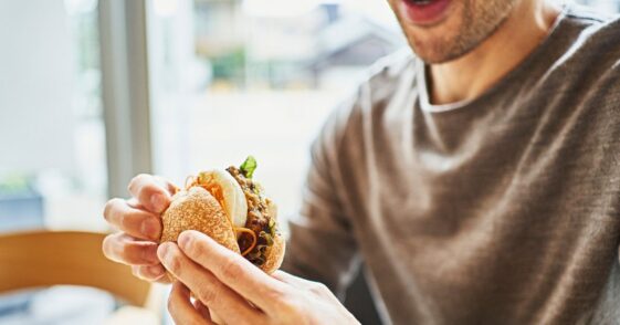 Asian man eating a veggie burger at a vegan cafe.