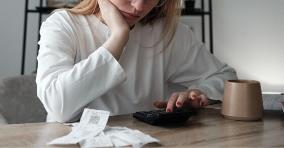 A young woman calculating spendings while looking at bills . She is using a calculator while sitting at the table.