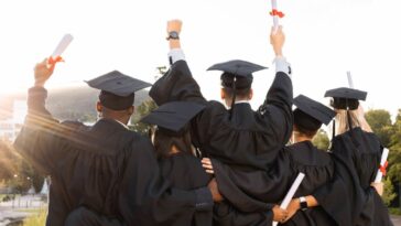 Wide shot, taken from the back of a group of excited students graduating in black robes.