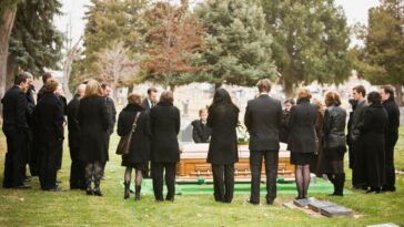 Shot of a group of mourners watching a coffin being lowered into the ground.