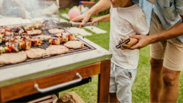 Photo of father and son grilling meat during a barbecue party in their yard.