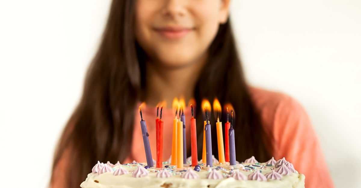 Portrait of joyful teen girl blowing candles on abirthday cake. White wall background.