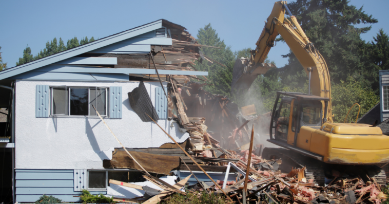 A house being torn down by a tractor.