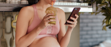 pregnant woman drinking iced coffee and looking at phone