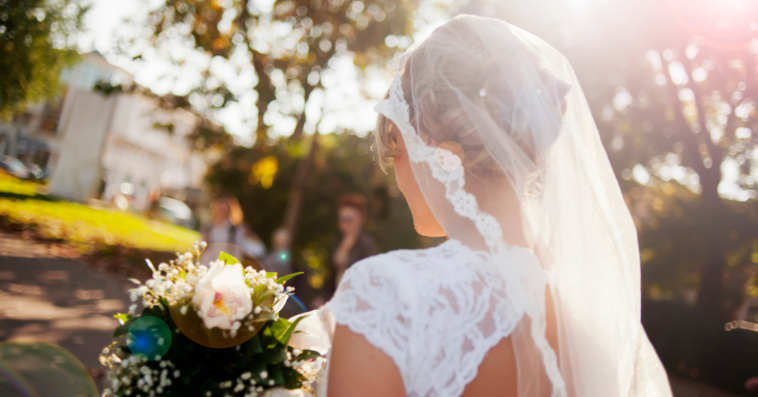 A bride seen from behind, walking outside.